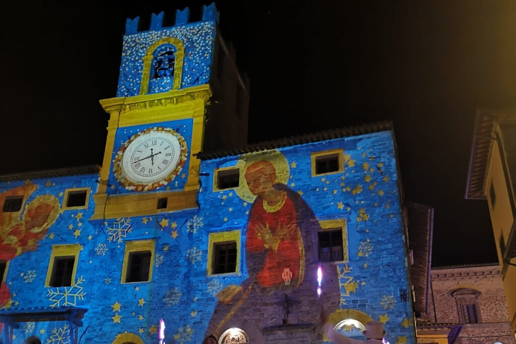Christmas light projections illuminating Palazzo Comunale in Piazza della Repubblica, Cortona, Tuscany, at night.